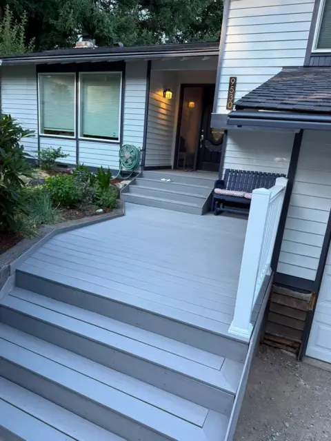Gray composite deck with steps and white post in a backyard